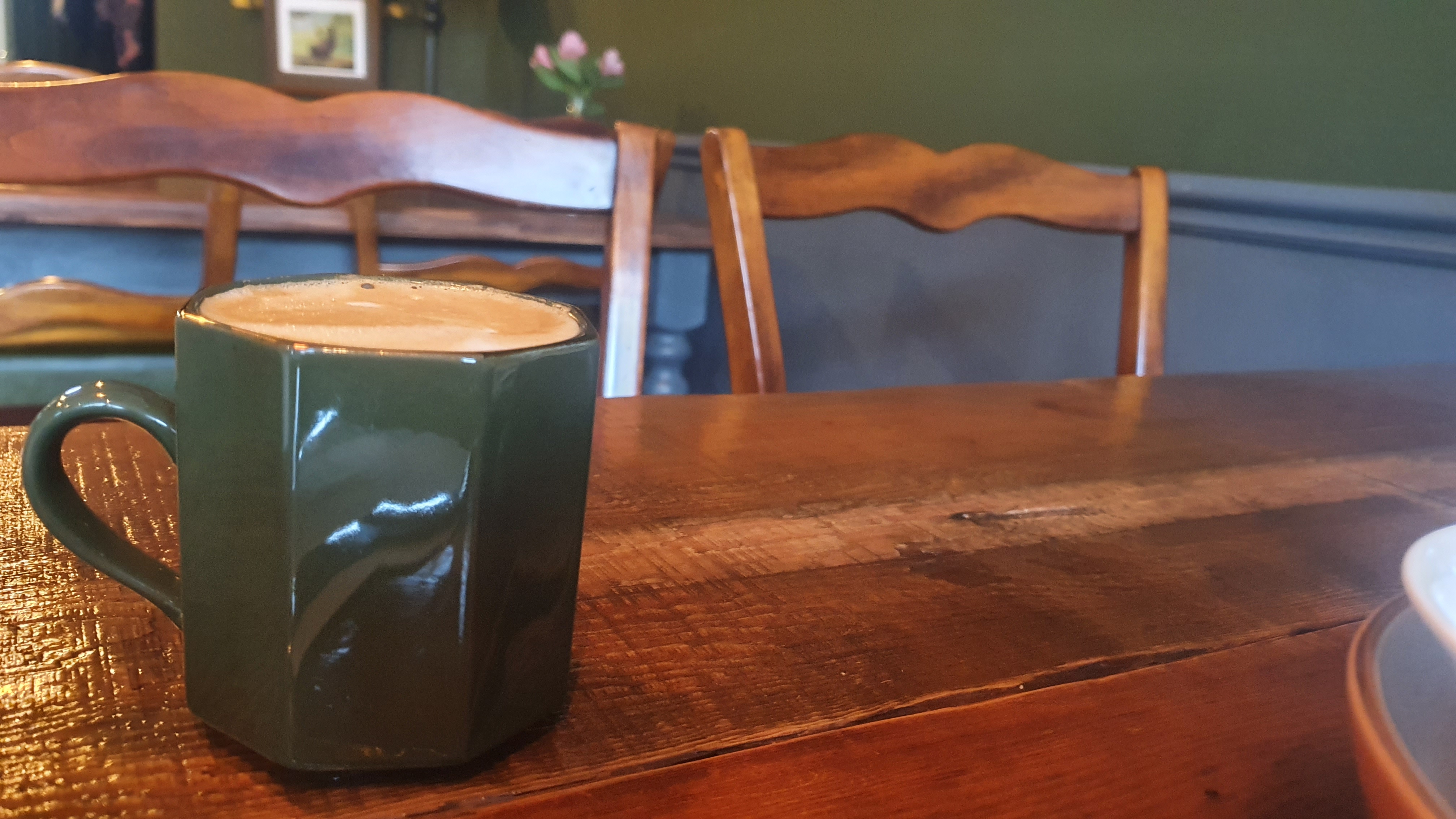 A green mug containing a foamy latte, on a wooden table in a cosy cafe